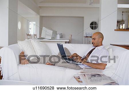 Man using laptop on couch View Large Photo Image Stock Photo - Man using laptop on couch. Fotosearch