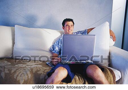 Stock Photo - Man using laptop on couch. Fotosearch