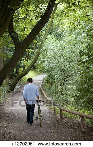 Man walking bike on dirt path View Large Photo Image Stock Image - Man walking bike on dirt path. Fotosearch