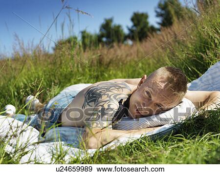 Stock Photo - Man with large tattoo laying in grass. Fotosearch