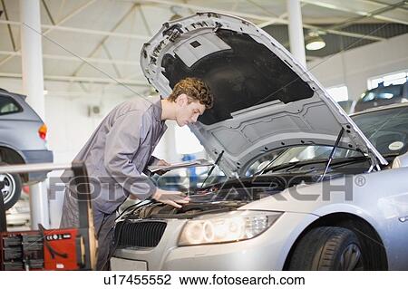 Mechanic examining car engine in garage View Large Photo Image Stock Image - Mechanic examining car engine in garage. Fotosearch