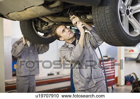 Stock Image - Mechanic working on car engine in garage. Fotosearch