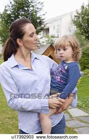 Stock Image - Mother holding daughter in backyard. Fotosearch