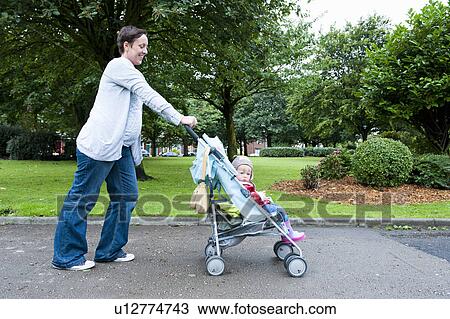 Stock Image - Mother pushing daughter in stroller. Fotosearch