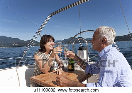 Stock Image - Older couple having champagne on boat. Fotosearch
