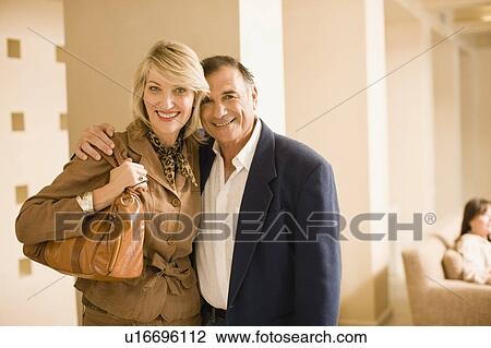 Stock Image - Older couple hugging in lobby area. Fotosearch