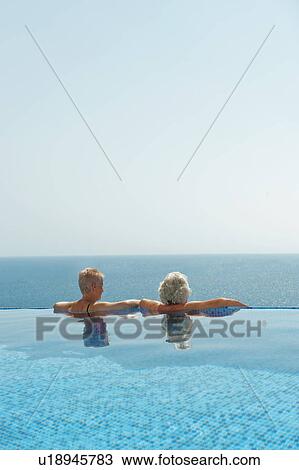 Stock Image - Older couple relaxing in infinity pool. Fotosearch