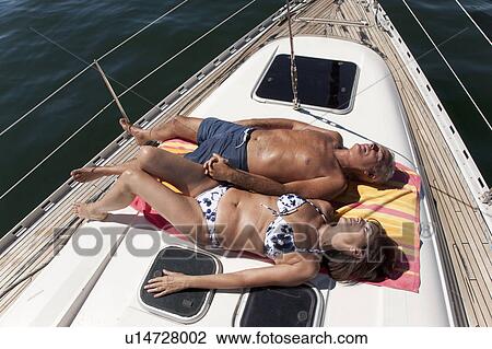 Stock Image - Older couple relaxing on sailboat. Fotosearch