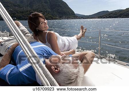 Stock Image - Older couple relaxing on sailboat. Fotosearch