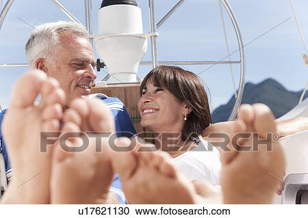 Stock Image - Older couple relaxing on sailboat. Fotosearch