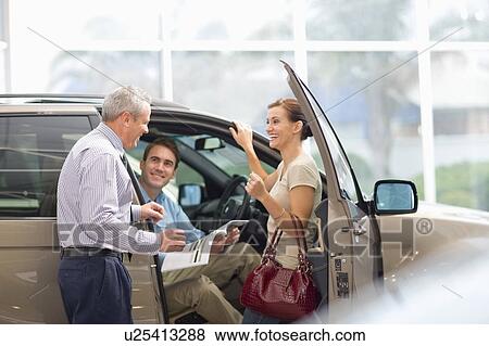 Stock Photo - Salesman showing off car in showroom. Fotosearch