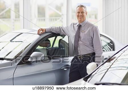 Salesman standing by car in showroom View Large Photo Image Stock Image - Salesman standing by car in showroom. Fotosearch