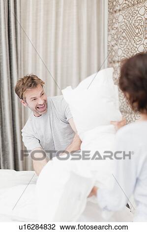 Smiling couple having pillow fight View Large Photo Image Stock Image - Smiling couple having pillow fight. Fotosearch
