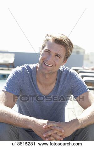 Stock Image - Smiling man sitting outdoors. Fotosearch
