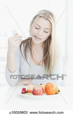 Stock Image - Smiling woman eating plate of fruit. Fotosearch