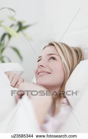 Picture - Smiling woman laying in bed. Fotosearch