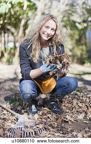 Stock Image - Smiling woman playing with dead leaves. Fotosearch