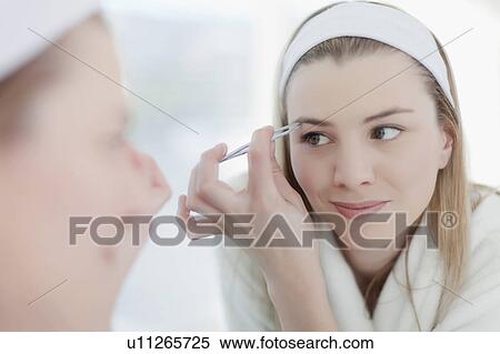 Stock Photography - Smiling woman plucking her eyebrows. Fotosearch