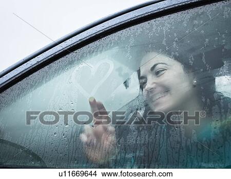 Picture - Teenage girl drawing on wet car window. Fotosearch