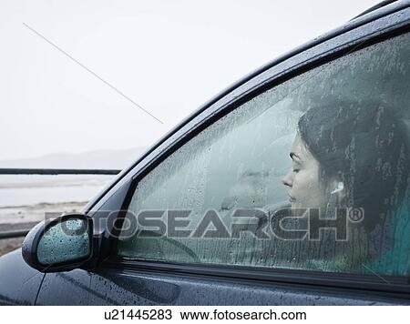 Stock Image - Teenage girl sitting in car by beach. Fotosearch