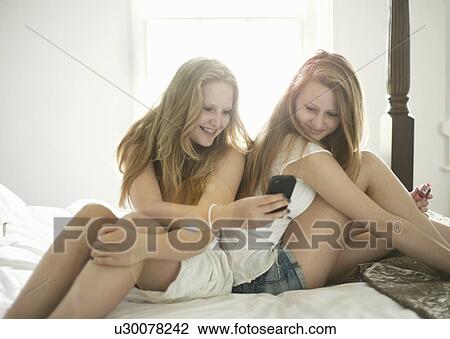 Teenage girls using cell phone on bed View Large Photo Image Stock Image - Teenage girls using cell phone on bed. Fotosearch