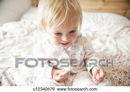 Stock Photo - Toddler girl eating in bed. Fotosearch