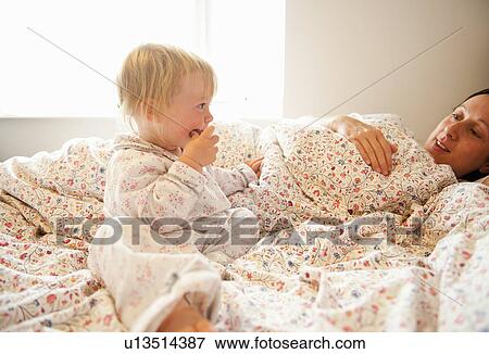 Stock Photo - Toddler girl sitting with mother in bed. Fotosearch