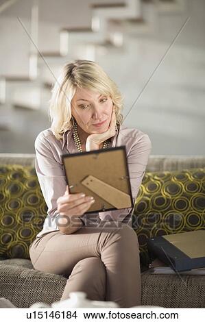 Picture - Woman admiring framed photo on couch. Fotosearch