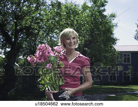 Stock Image - Woman carrying potted flowers outdoors. Fotosearch
