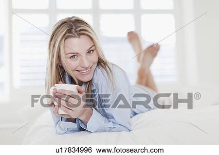 Woman drinking cup of coffee on bed View Large Photo Image Stock Photograph - Woman drinking cup of coffee on bed. Fotosearch