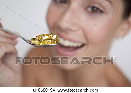 Picture - Woman eating spoonful of supplements. Fotosearch