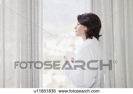 Stock Photography - Woman in bathrobe looking out window. Fotosearch