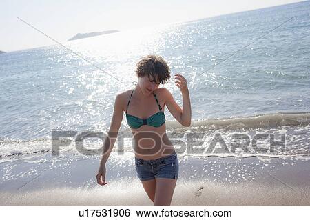 Stock Photograph - Woman in bikini walking on beach. Fotosearch