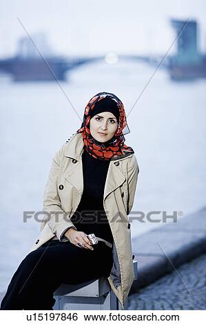 Stock Photograph - Woman in headscarf sitting on bench. Fotosearch