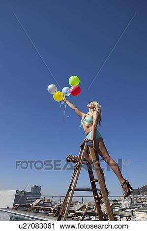 Stock Image - Woman in swimsuit with bunch of balloons. Fotosearch