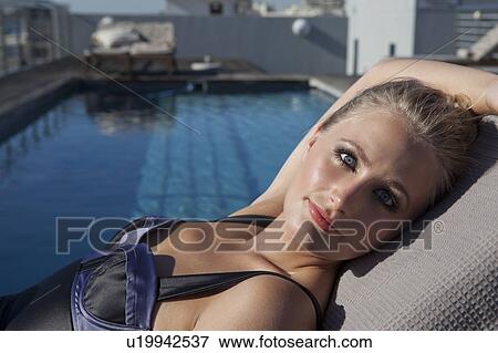 Stock Photo - Woman laying in lawn chair by pool. Fotosearch