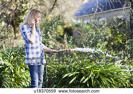 Stock Photo - Woman on cell phone watering plants. Fotosearch