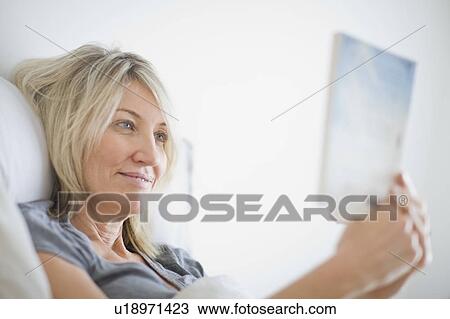 Stock Image - Woman reading book in bed. Fotosearch