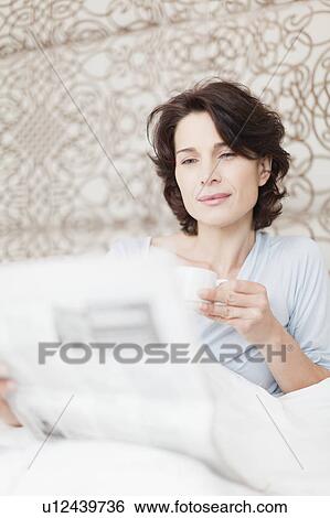 Stock Photograph - Woman reading newspaper in bed. Fotosearch