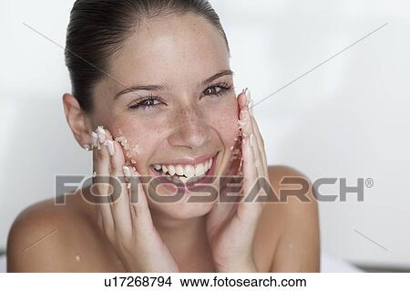 Picture - Woman scrubbing sugar on her face. Fotosearch
