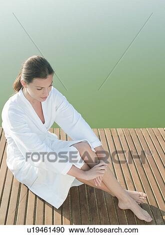 Stock Image - Woman sitting on dock of lake. Fotosearch