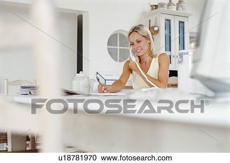 Stock Image - Woman talking on phone in kitchen. Fotosearch