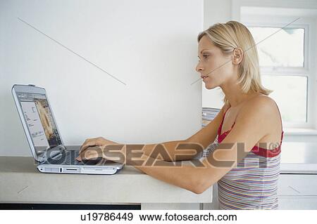 Stock Photo - Woman using laptop on mantelpiece. Fotosearch