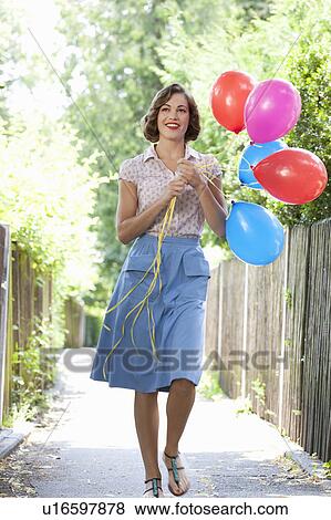 Stock Photo - Woman with balloons on suburban street. Fotosearch