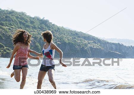 Women running in waves on beach View Large Photo Image Stock Photo - Women running in waves on beach. Fotosearch
