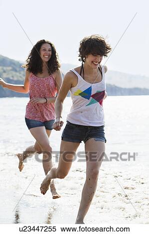 Stock Photography - Women running in waves on beach. Fotosearch