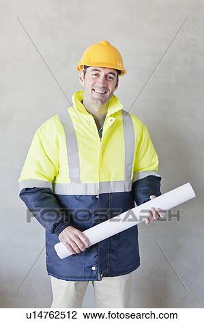 Stock Image - Worker carrying blueprints on site. Fotosearch