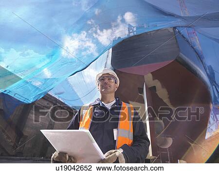 Worker reading on shipbuilding site View Large Photo Image Stock Image - Worker reading on shipbuilding site. Fotosearch