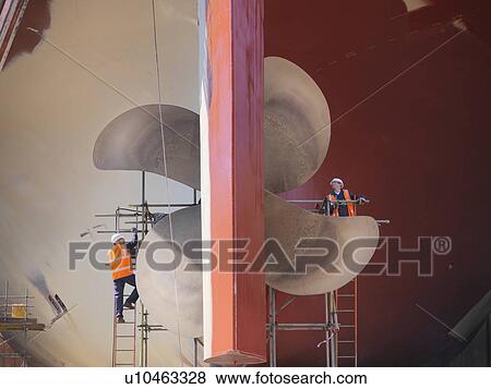 Stock Photo - Workers examining ship turbines on site. Fotosearch