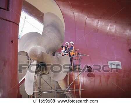 Stock Photo - Workers examining ship turbines on site. Fotosearch